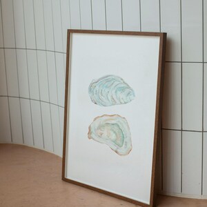 Puede incluir: Una pintura de acuarela enmarcada de dos conchas de ostra. Las conchas est&aacute;n pintadas en tonos de azul, verde y marr&oacute;n. La pintura est&aacute; sobre un fondo blanco.