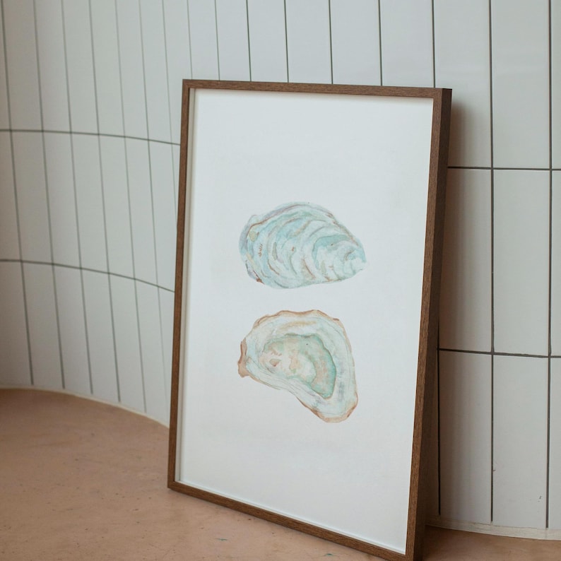Puede incluir: Una pintura de acuarela enmarcada de dos conchas de ostra. Las conchas est&aacute;n pintadas en tonos de azul, verde y marr&oacute;n. La pintura est&aacute; sobre un fondo blanco.