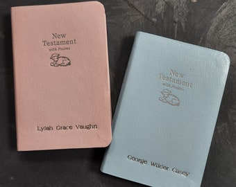 May include: Two personalized New Testaments with Psalms, one in pink with the name Lylah Grace Vaughn and one in blue with the name George Wilder Casey.
