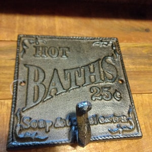 May include: Cast iron wall hook with a sign that reads "HOT BATHS 25c" and "Soap & towels extra".