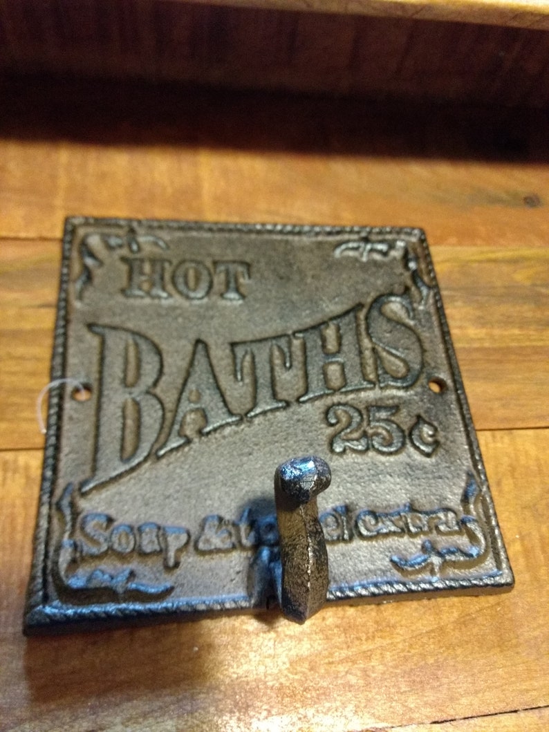 May include: Cast iron wall hook with a sign that reads "HOT BATHS 25c" and "Soap & towels extra".