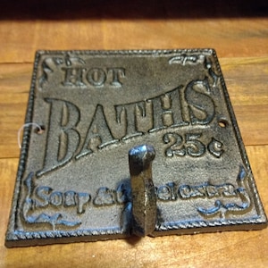 May include: Cast iron sign with the text "HOT BATHS 25c" and a hook. The sign is brown and has a distressed look.