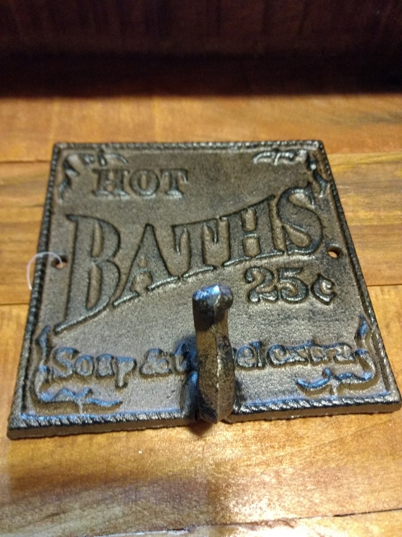 May include: Cast iron sign with the text "HOT BATHS 25c" and a hook. The sign is brown and has a distressed look.