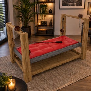 May include: A wooden frame bench featuring a tufted red leather-like padded seat, gray metal support beams, and four brown leather cuffs attached to the frame by silver-colored metal chains. A black leather whip rests on the red seat surface.