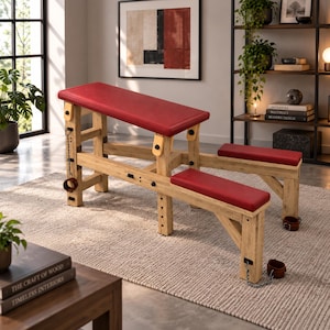 May include: A wooden furniture piece featuring a multi-level design with red padded surfaces. The structure includes adjustable supports, metal chains, and brown leather-like cuffs attached to the frame, providing a functional platform for various uses.