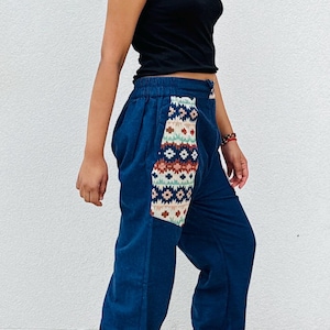Könnte beinhalten: Dunkelblaue Cordhose mit einem gemusterten Aufnäher an der Seite. Der Aufnäher zeigt geometrische Designs in Braun-, Weiß- und Rottönen. Die Hose hat einen elastischen Bund und Bündchen. Ein schwarzes Tanktop ist ebenfalls zu sehen.