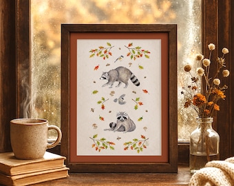 May include: A framed watercolor print featuring two raccoons, birds, and autumn leaves. The artwork is set against a neutral background and framed in dark brown wood. The print is displayed on a wooden surface with a cup of coffee and books.
