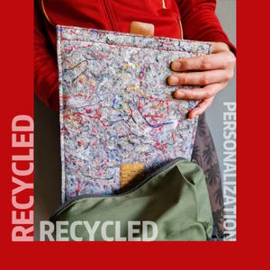 Könnte beinhalten: Eine graue Laptoptasche aus recycelten Materialien mit bunten Fäden und einem Ledergriff. Die Tasche ist geöffnet und zeigt eine grüne Tasche. Das Wort "RECYCLED" ist vertikal und horizontal gedruckt.