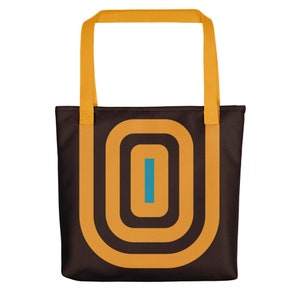 May include: A brown tote bag with a yellow handle and a geometric design featuring concentric circles in yellow and a blue vertical line in the centre.