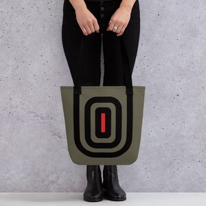 May include: A green tote bag with black straps and a black and red geometric design. The design features a series of concentric circles with a red line in the center.