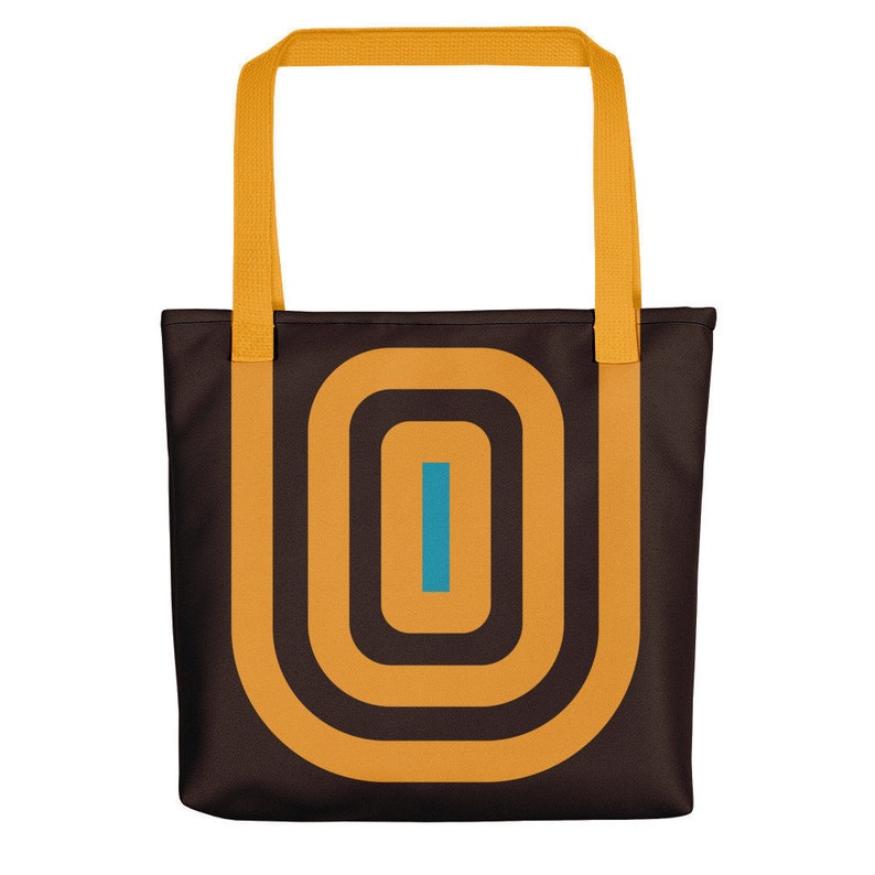 May include: A brown tote bag with a yellow handle and a geometric design featuring concentric circles in yellow and a blue vertical line in the centre.