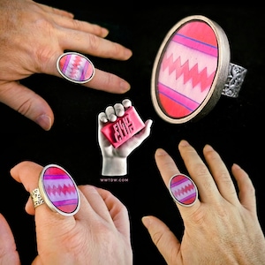 May include: Three silver rings with pink and white oval-shaped stones featuring a zig-zag pattern. The rings are on different hands. A pink bar of soap with the words "Fight Club" is in the background.