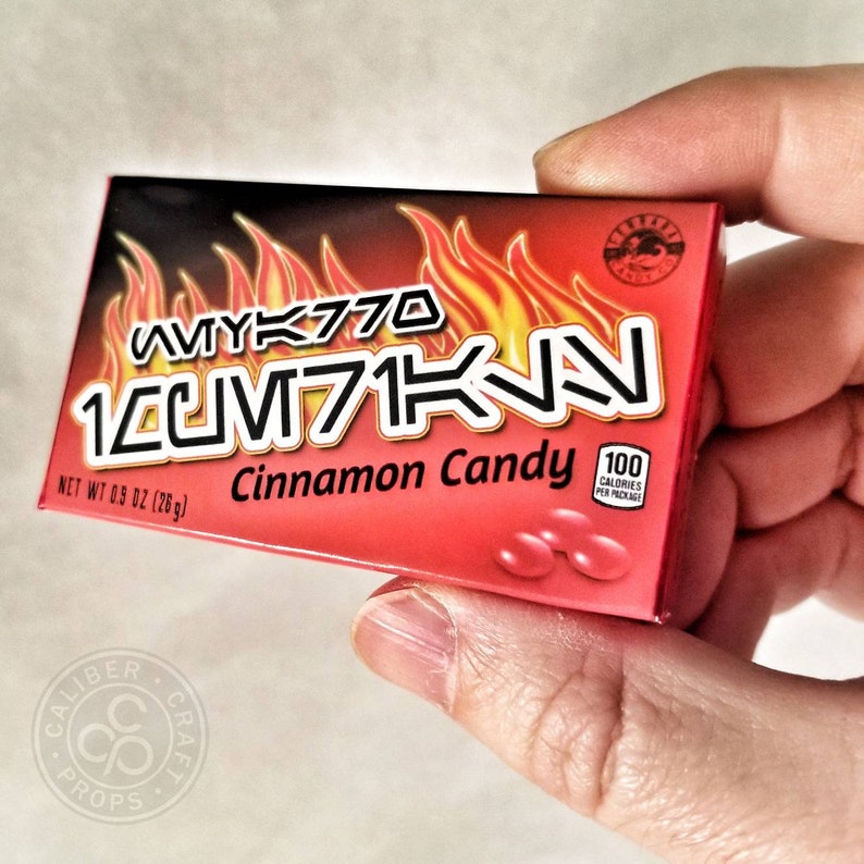 May include: A red box of "10CM71KN" cinnamon candy, with flames graphic and the text "AVYK770". The box contains 0.9 oz (28g) of candy and 100 calories per package.
