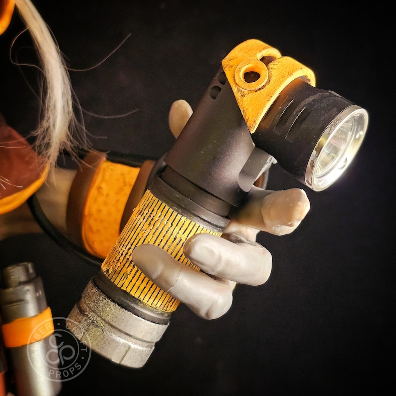 May include: A handheld torch with a black body and a yellow, textured grip section. The head of the torch is angled, featuring a yellow frame and a metallic silver rim around the lens. The design includes weathered, distressed details.