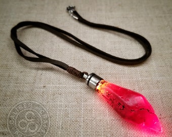 May include: A red glass pendant shaped like a teardrop with a silver metal cap hangs from a brown leather cord. The pendant is illuminated from within, creating a glowing effect.