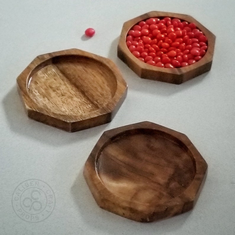 May include: Three wooden, octagonal trays. One tray is filled with small, red candies. The trays are made of a light brown wood with a smooth finish. The trays are empty, except for the one filled with candies.