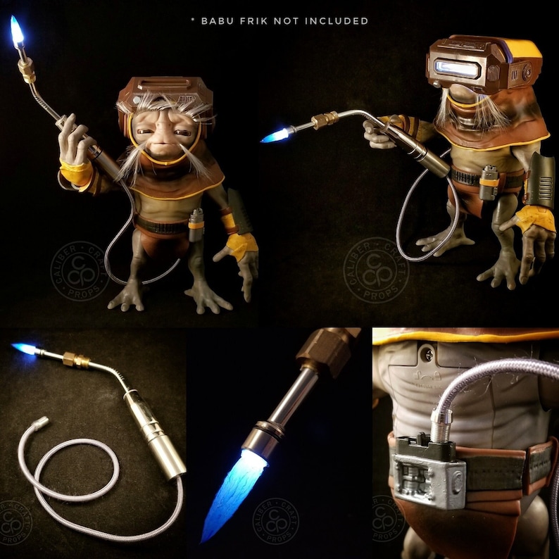 May include: A detailed replica of a welding torch from the Star Wars series The Mandalorian. The torch is made of metal and has a blue light at the tip. The torch is connected to a hose and a handle. The text "BABU FRIK NOT INCLUDED" is visible in the image.