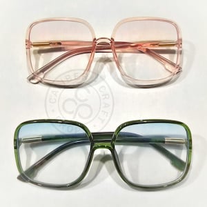 May include: Two pairs of square-framed sunglasses. One pair has a translucent pink frame and gradient pink lenses. The other pair has a green frame and gradient blue lenses. Both have gold-colored accents.