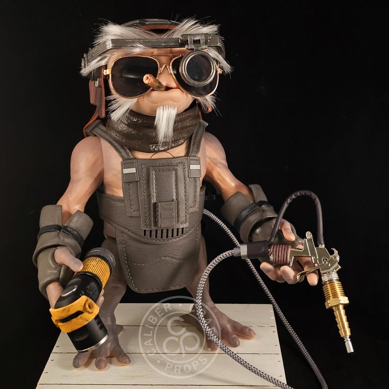 May include: A detailed sculpture of a humanoid alien figure wearing goggles, sunglasses, and a utility vest. The figure holds a black and yellow cylindrical object in one hand and a metallic spray gun in the other. The figure has a white beard and is smoking a cigar.