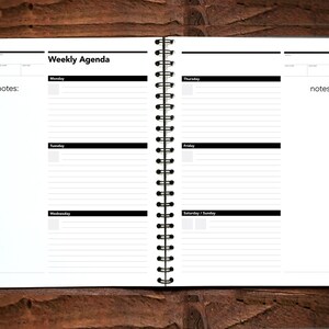 May include: A white weekly agenda planner with a black spiral binding. The planner has sections for each day of the week, Monday through Sunday, with space for notes.
