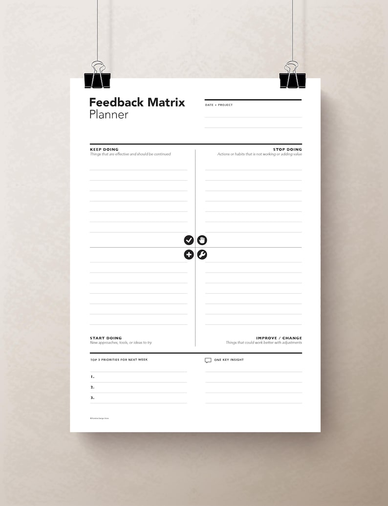 May include: A white Feedback Matrix Planner sheet, held by black binder clips. The planner includes sections for keeping, stopping, starting, and improving actions, with space for notes and priorities. The text is in black.