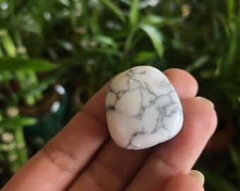 Könnte beinhalten: Weißer Howlith-Trommelstein mit grauen Adern. Der Stein ist glatt und poliert.