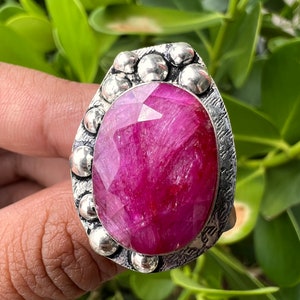 May include: A silver ring with a large, faceted, pink gemstone set in a textured bezel. The ring is surrounded by small, round silver beads.