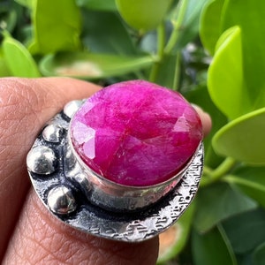 May include: A silver ring featuring a large, oval-shaped pink gemstone set in a textured silver band.