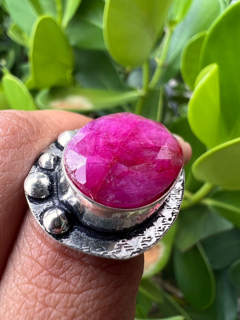 May include: A silver ring featuring a large, oval-shaped pink gemstone set in a textured silver band.