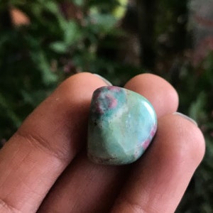 May include: A green and pink tumbled stone with a smooth, polished surface.