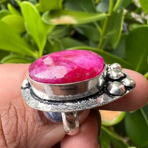 May include: A silver ring featuring a large, oval-shaped pink gemstone set in a bezel setting. The ring has a textured band and a decorative design on the side.