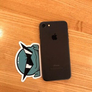 May include: A black iPhone with a sticker of a green cartoon creature with a lightning bolt on its head.