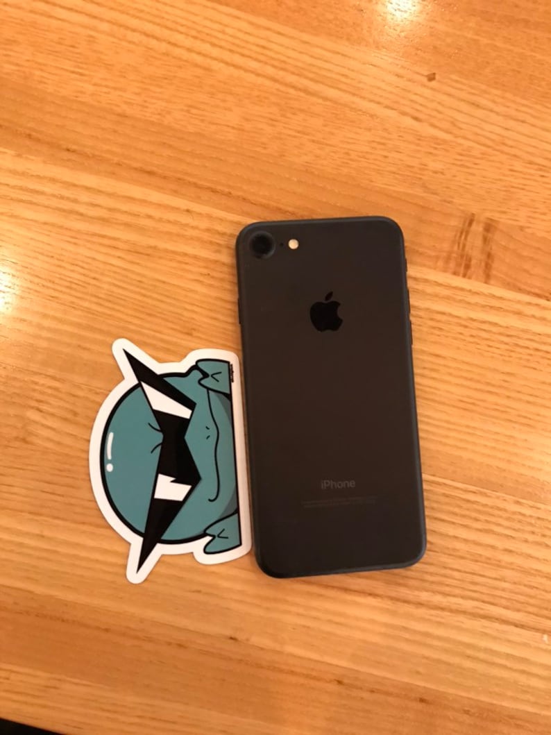 May include: A black iPhone with a sticker of a green cartoon creature with a lightning bolt on its head.