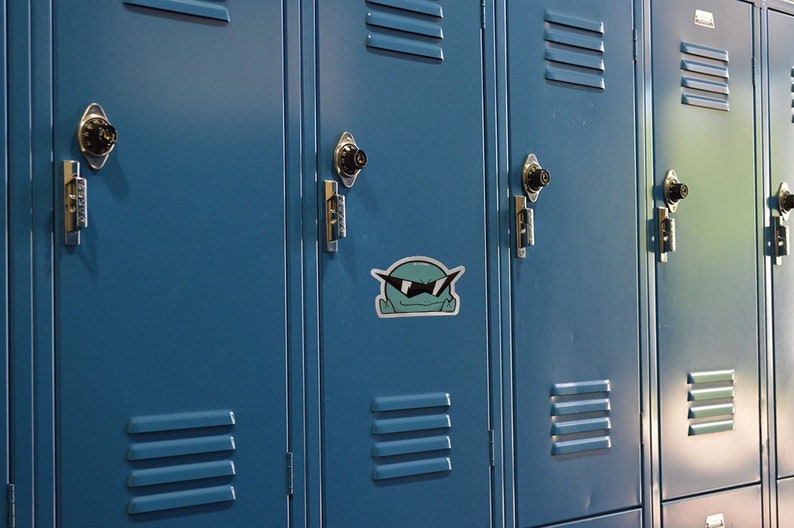 May include: A row of blue metal lockers with a cartoon sticker of a green creature wearing sunglasses on one of the lockers.