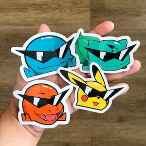 May include: Four cartoon character stickers with sunglasses. The characters are a blue, green, yellow, and orange. The stickers are on a wooden surface.