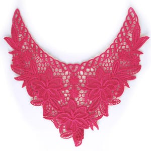 May include: A V-shaped hot pink lace collar appliqué featuring an intricate floral pattern with embroidered petals and leaves connected by a delicate openwork mesh design. The piece is symmetrical with pointed ends and a central floral motif.