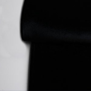 Pu&ograve; includere: Un primo piano di un tessuto nero piegato a met&agrave;. Il tessuto ha una texture liscia e vellutata.
