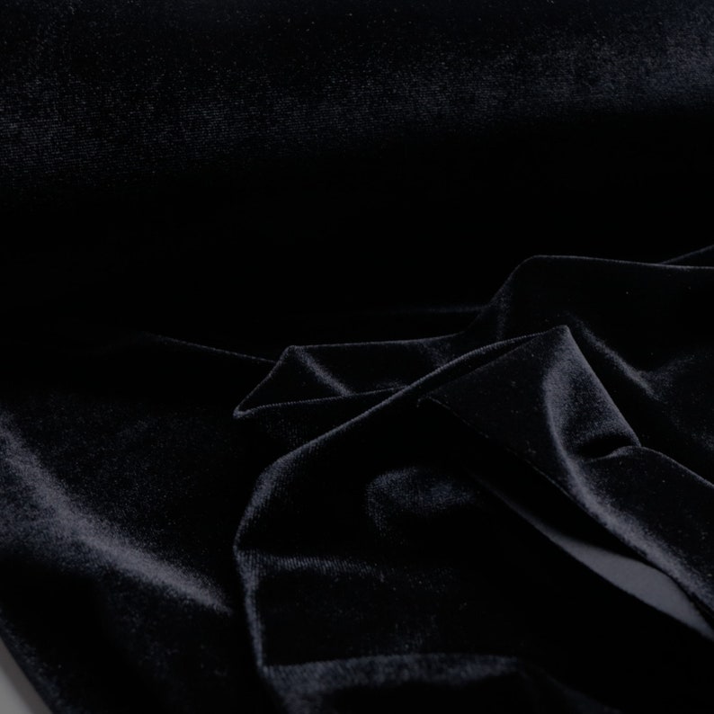 Pu&ograve; includere: Tessuto di velluto nero con una texture morbida e liscia. Il tessuto &egrave; piegato e drappeggiato, mostrando la sua sensazione di lusso.