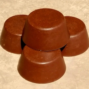 May include: Four solid, round, brown bars of soap arranged in a pyramid stack. Each bar has a smooth, slightly tapered cylindrical shape with a flat top and a solid, uniform dark brown color throughout the entire surface of the objects.