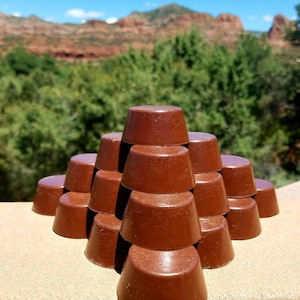 May include: A pyramid of 15 brown chocolate discs stacked on a light brown surface. The chocolate discs are smooth and shiny.