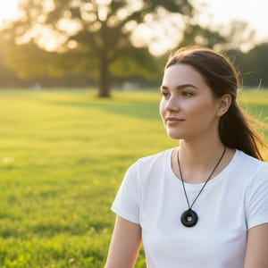 Black Sun Orgonite donut pendant necklace worn outdoors in a natural park setting. Handmade circular orgonite pendant displayed on a black cord necklace. Lifestyle image showing comfortable everyday wear in an outdoor environment.