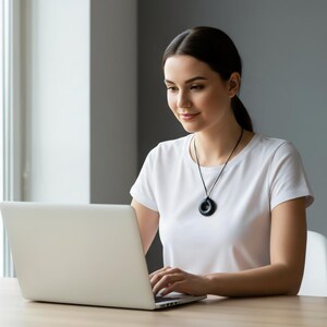 Woman wearing a Black Sun Orgonite donut pendant necklace while working on a laptop. Handmade orgonite jewelry featuring a round donut design and black finish. Lifestyle photo demonstrating everyday wear at home, work, or office environments.
