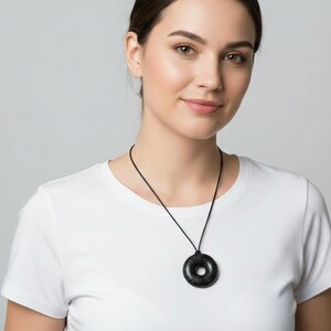 Woman wearing a Black Sun Orgonite donut pendant necklace on a black cord. Handmade orgonite jewelry shown at chest level for size reference. Lightweight round pendant with a polished black finish suitable for everyday wear.