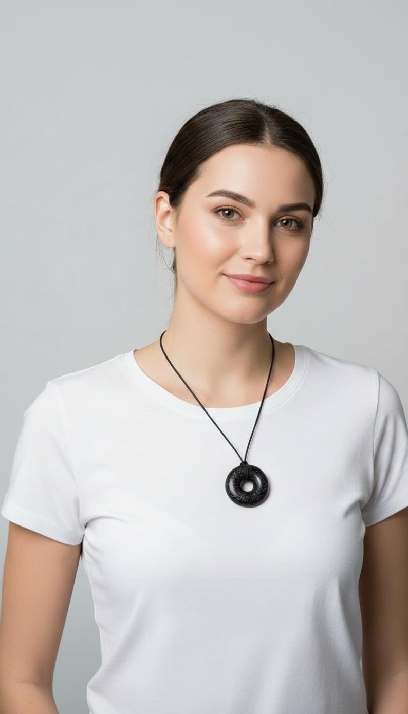 Woman wearing a Black Sun Orgonite donut pendant necklace on a black cord. Handmade orgonite jewelry shown at chest level for size reference. Lightweight round pendant with a polished black finish suitable for everyday wear.