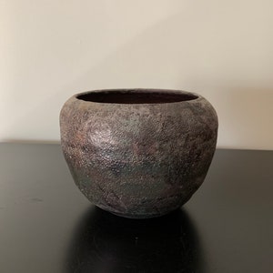 May include: A dark gray ceramic planter with a textured surface. The planter has a rounded shape and a wide opening.