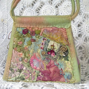 Puede incluir: Un bolso de mano de patchwork verde y rosa con bordados florales y lentejuelas. El bolso tiene un asa superior y está hecho de fieltro.
