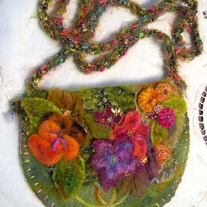 May include: A green felt purse with a floral design. The purse has a long, colourful crocheted strap. The flowers are made of felt and are in shades of orange, red, purple, and green.