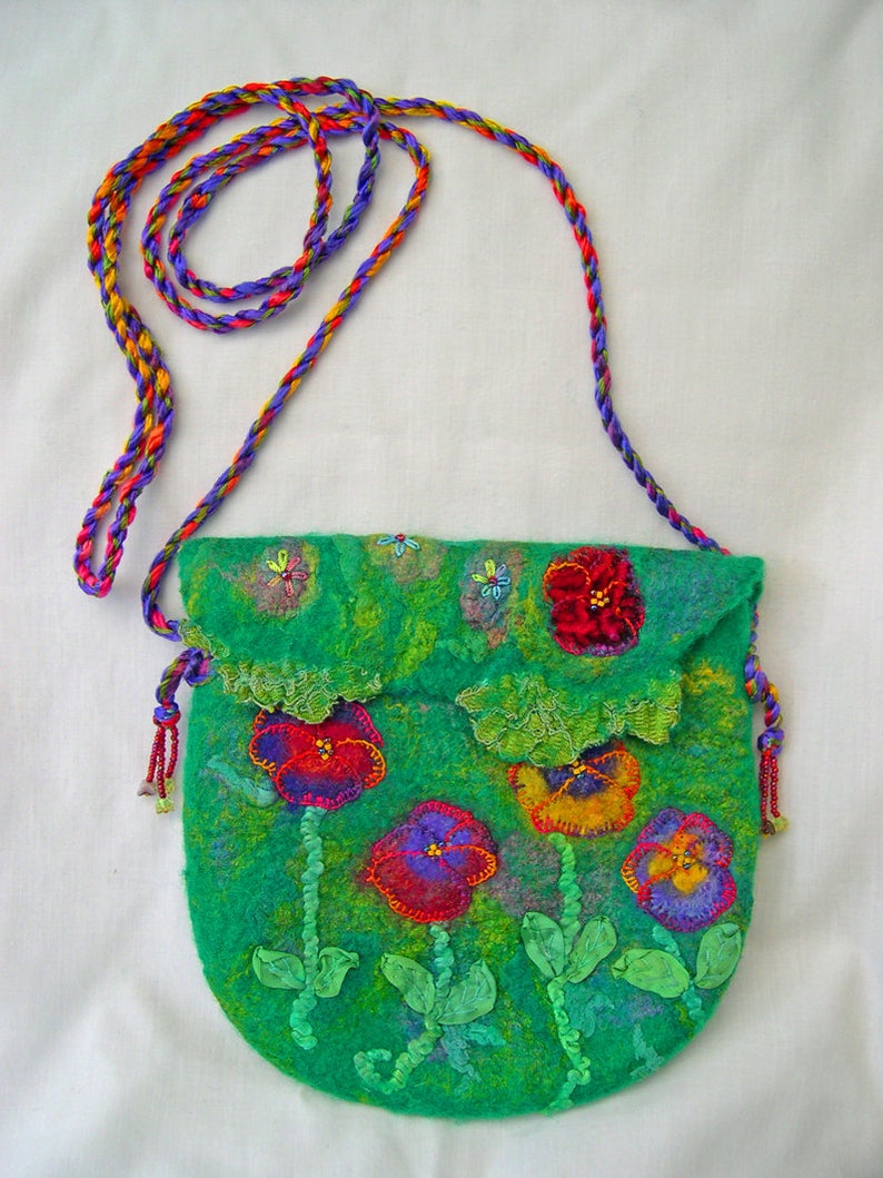 May include: A green felt purse with a floral design. The purse has a long strap made of braided purple, red, and yellow yarn. The flowers are embroidered with red, yellow, and purple thread. The purse is decorated with green leaves and beads.