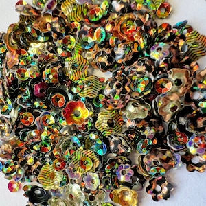 May include: A large assortment of iridescent flower-shaped sequins in shades of gold, red, green, and black.