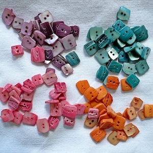 May include: Assortment of colorful shell buttons in pink, orange, teal and purple. The buttons are all square shaped with two holes.